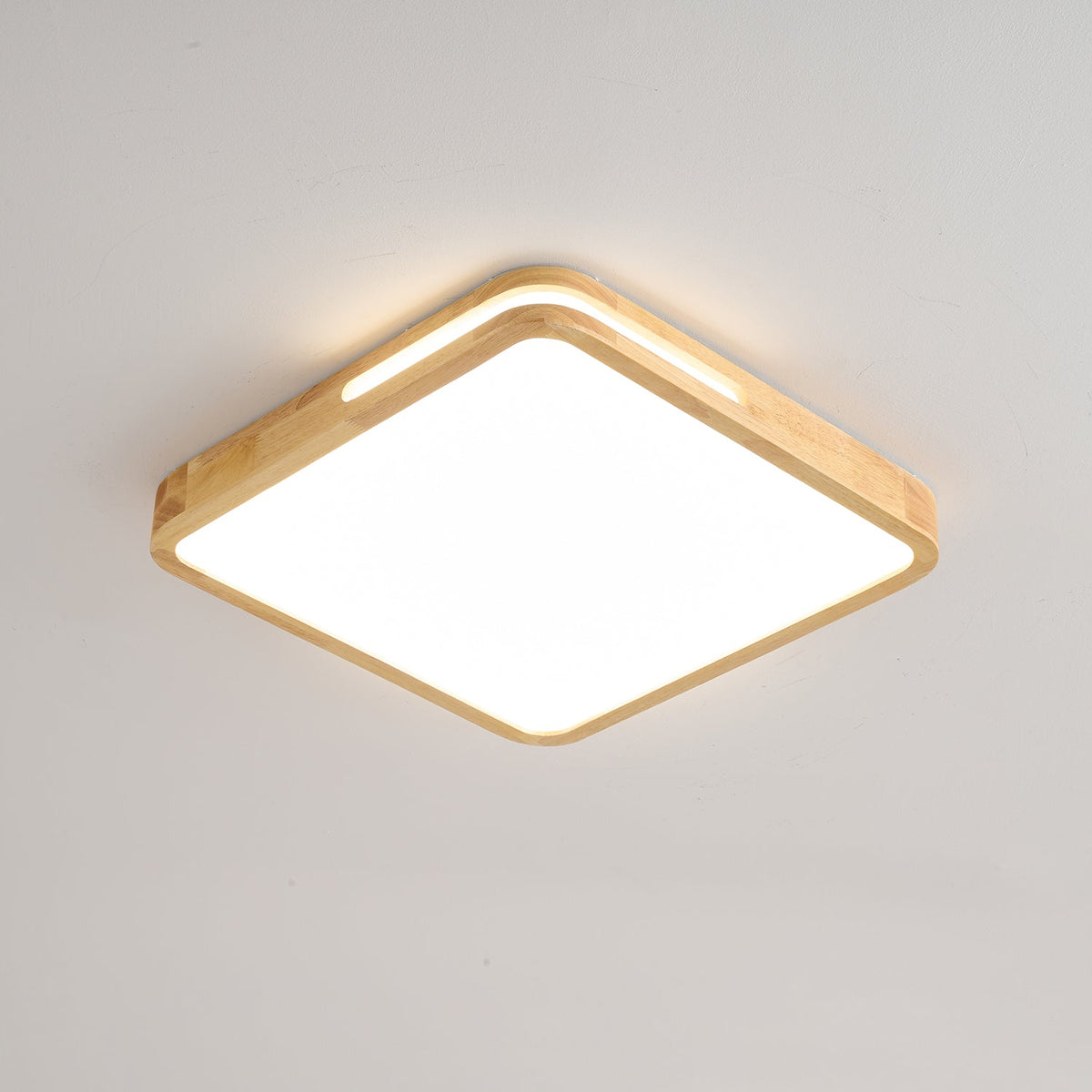 Square Clérachic ceiling light in a light wood finish, switched on, with a glow spilling from the slot in the frame.