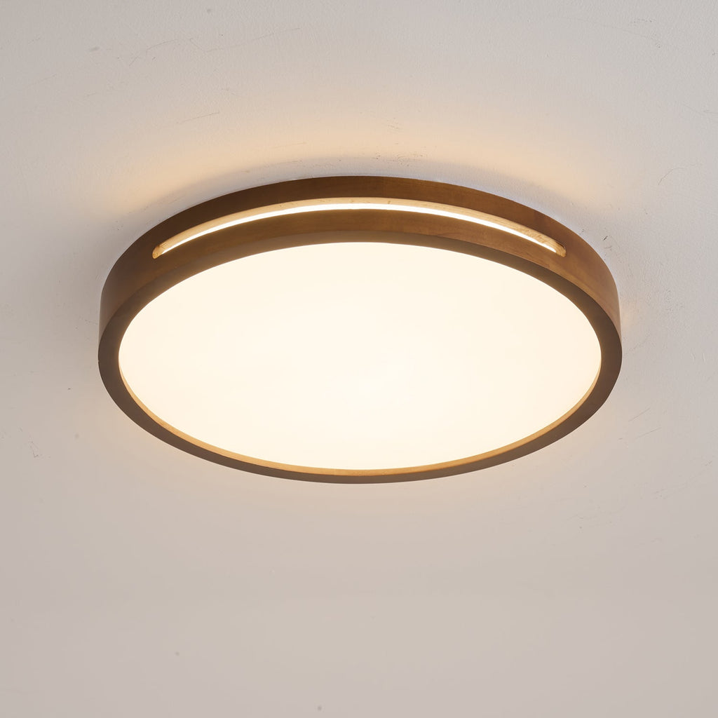Round walnut ceiling light from Clérachic with a warm glow through the rim slot and a bright frosted panel below.