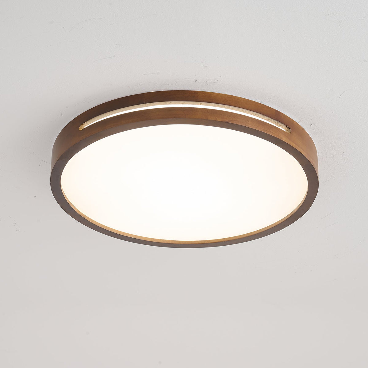 Round dark wood Clérachic ceiling light, lit, with a slim slot in the frame and an even white glow across the panel.