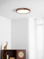 A small round walnut ceiling light from Clérachic in a white room with sheer curtains and a dark wooden cabinet.