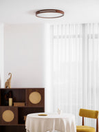 Distant round walnut ceiling light from Clérachic above a room with a set round table, a yellow chair and a rattan cabinet.