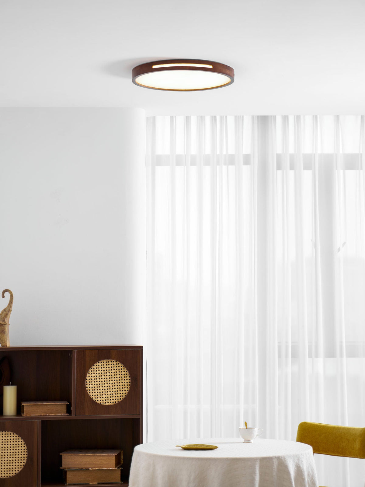 Lit round walnut Clérachic ceiling light above a rattan-door sideboard, with sheer white curtains behind it.