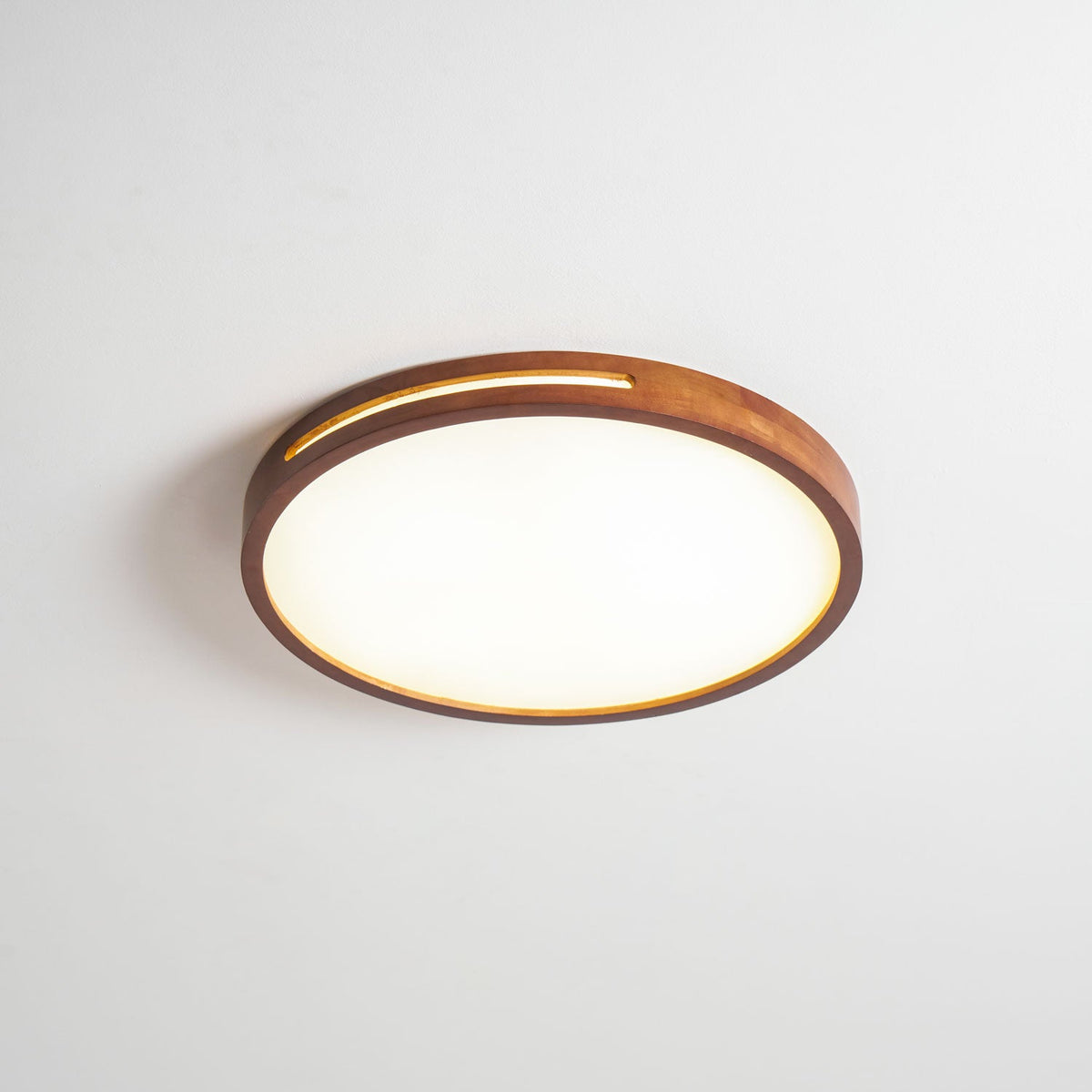 Round walnut-frame ceiling light from Clérachic, lit, with light showing along the rim slot and a bright white panel.