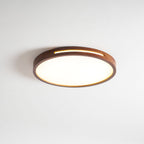 Side-on view of a lit round walnut Clérachic ceiling light, with a warm strip of light through the slot in its frame.