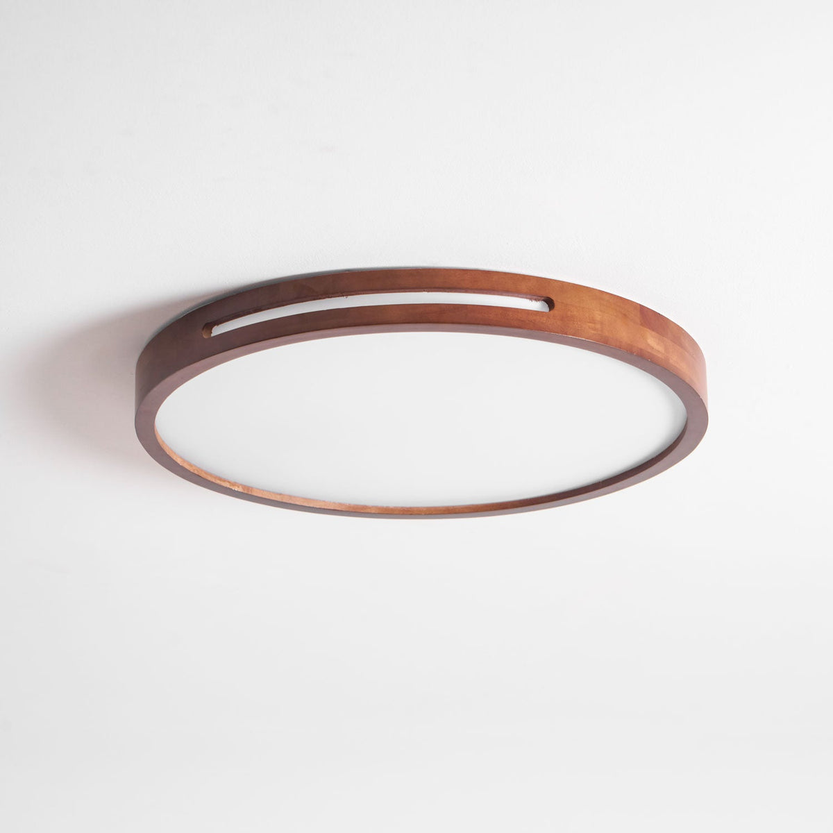 Unlit round walnut ceiling light from Clérachic on a white ceiling, with the slot in its frame and a frosted panel.