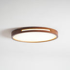 Low-angle view of a lit round walnut Clérachic ceiling light, with a gold glow along the slot and the shallow frame.