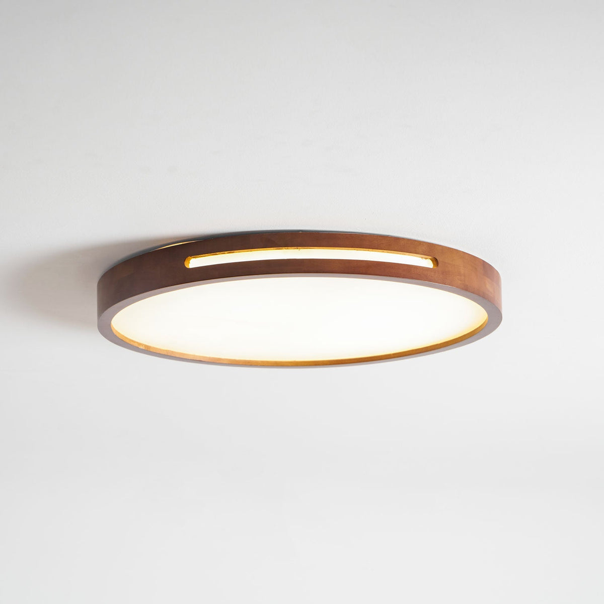 Low-angle view of a lit round walnut Clérachic ceiling light, with a gold glow along the slot and the shallow frame.