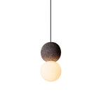 This Clérachic pendant, a dark textured sphere above a glowing opal glass globe, hangs against a plain white background.