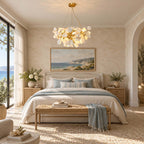 A Clérachic chandelier above a bed dressed in pale blue, with a woven bench, an arched doorway and a sea view outside.