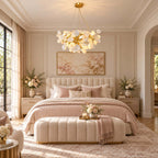 The Clérachic chandelier hangs over a blush-pink bed with a channelled ottoman, in a cream room with an arched window.