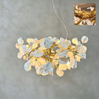 The Clérachic chandelier lit against a grey plaster wall, its ceramic petals clustered on a gold vine, with a small detail inset.