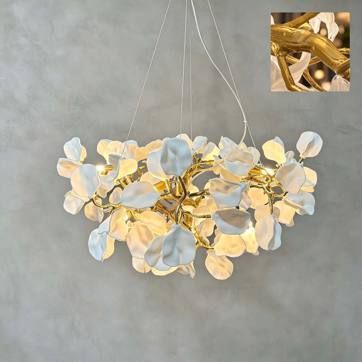 A Clérachic chandelier lit against a grey wall, with soft white ceramic petals on a gold vine and an inset close-up of the branch.