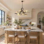 A Clérachic branch chandelier lit above a marble kitchen island with rattan bar stools, beneath white cabinets and an arched opening.