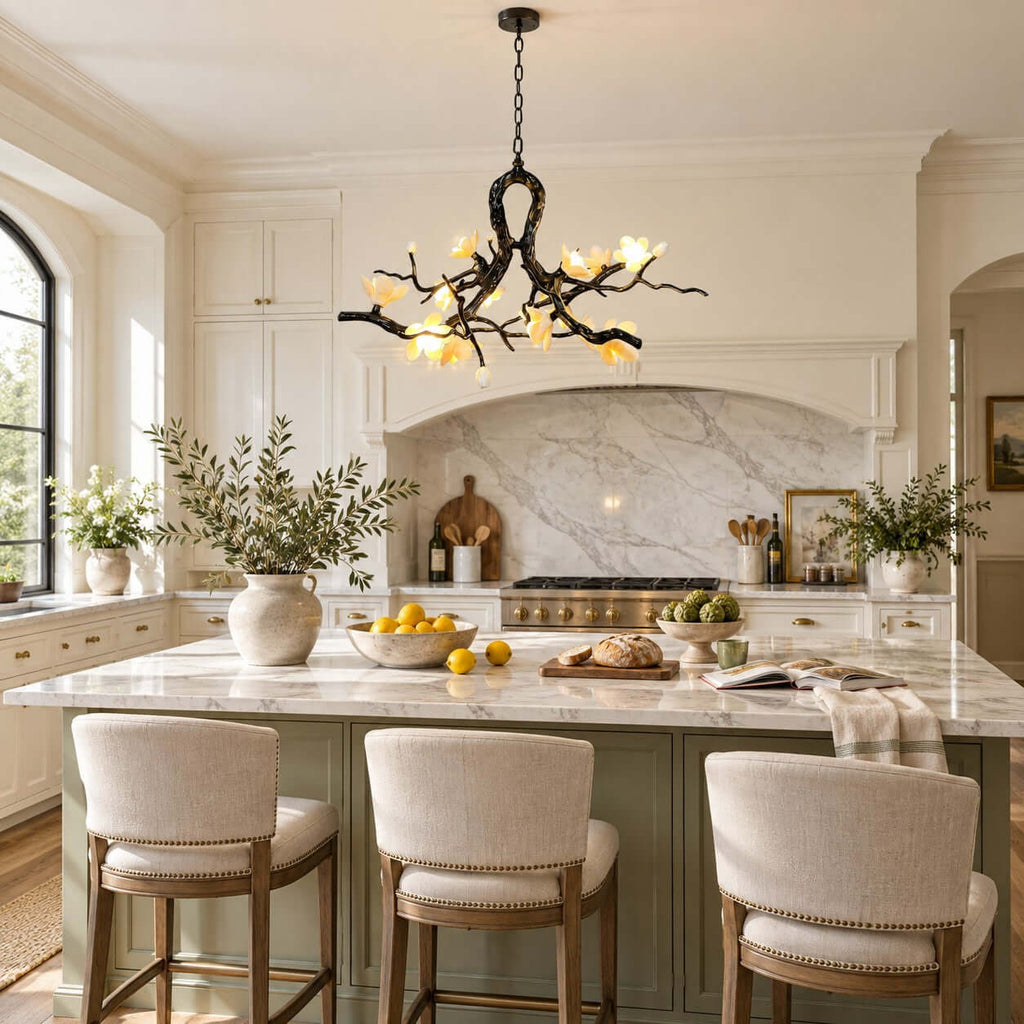 Lit Clérachic chandelier with ceramic blooms hung over a kitchen island with cream bar stools, a marble splashback behind.