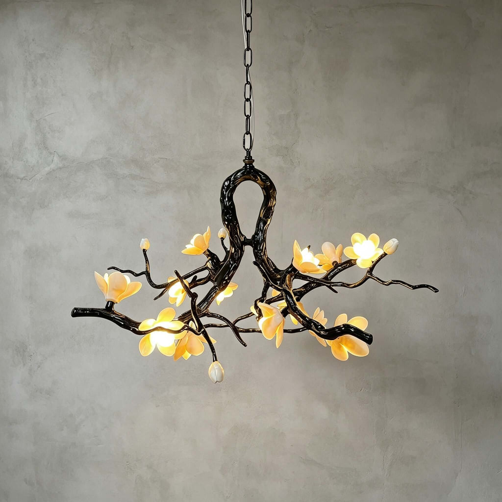 Lit Clérachic chandelier against a grey plaster wall, its dark vine frame glowing with warm yellow ceramic blooms and a few buds.