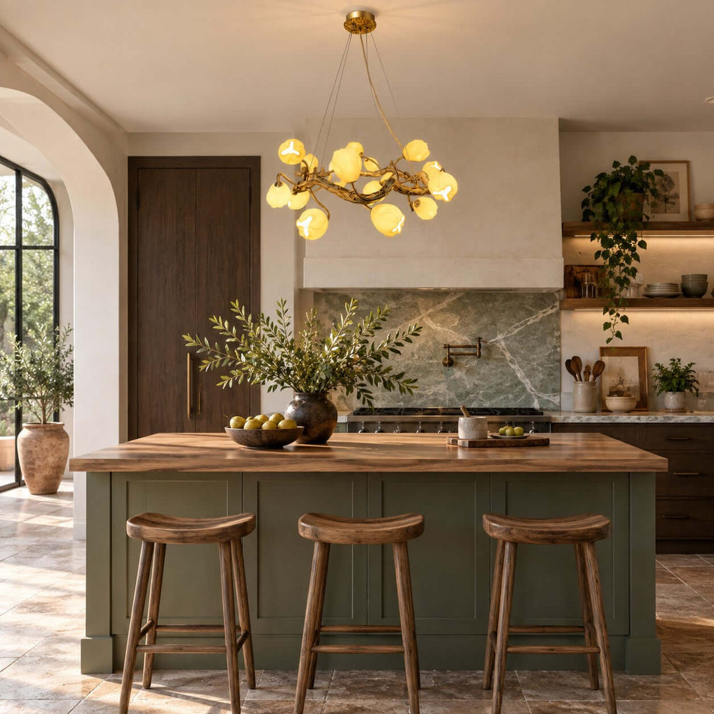 This Clérachic gold flower chandelier hangs over a green kitchen island with three wooden stools and a marble splashback behind.