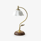 White ceramic flower-shaped shade on a curved brass-toned arm with a leaf detail, set on a round walnut-effect base, from Clérachic.