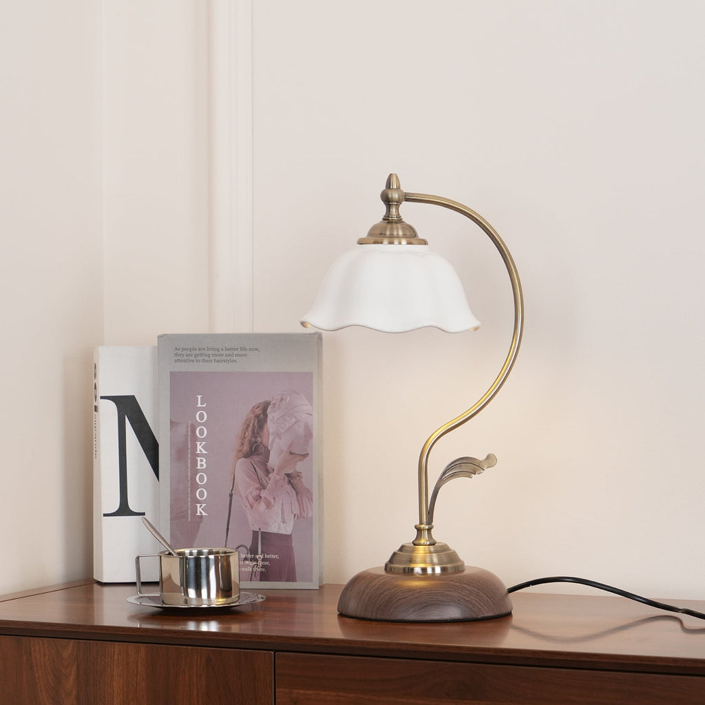 Softly lit Clérachic table lamp with a frilled white shade, standing on a wooden sideboard against a pale wall with books behind.
