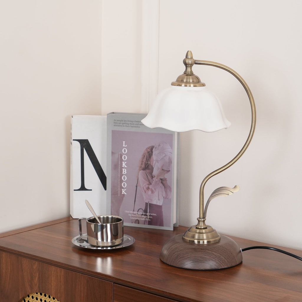 Low view of this Clérachic table lamp on a wooden cabinet, its curved arm and round wood-grain base beside a stack of books and a cup.