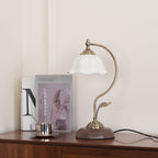 Clérachic lamp with a fluted white ceramic shade beside a lookbook and a steel cup on a dark wood sideboard.