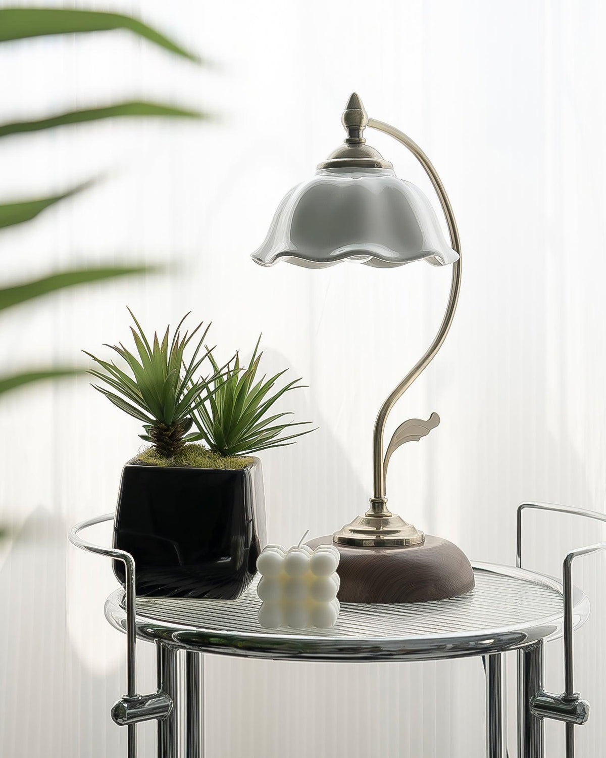 This Clérachic table lamp on a glass side table, next to a green plant in a black pot and a small bubble-shaped candle.