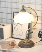 Lit Clérachic table lamp with a glowing frosted shade, set on a white desk in front of a framed line drawing and a cream speaker.