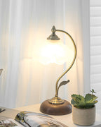 Frosted shade of this Clérachic table lamp aglow against a sheer curtain, with a succulent in a woven pot and a magazine below.
