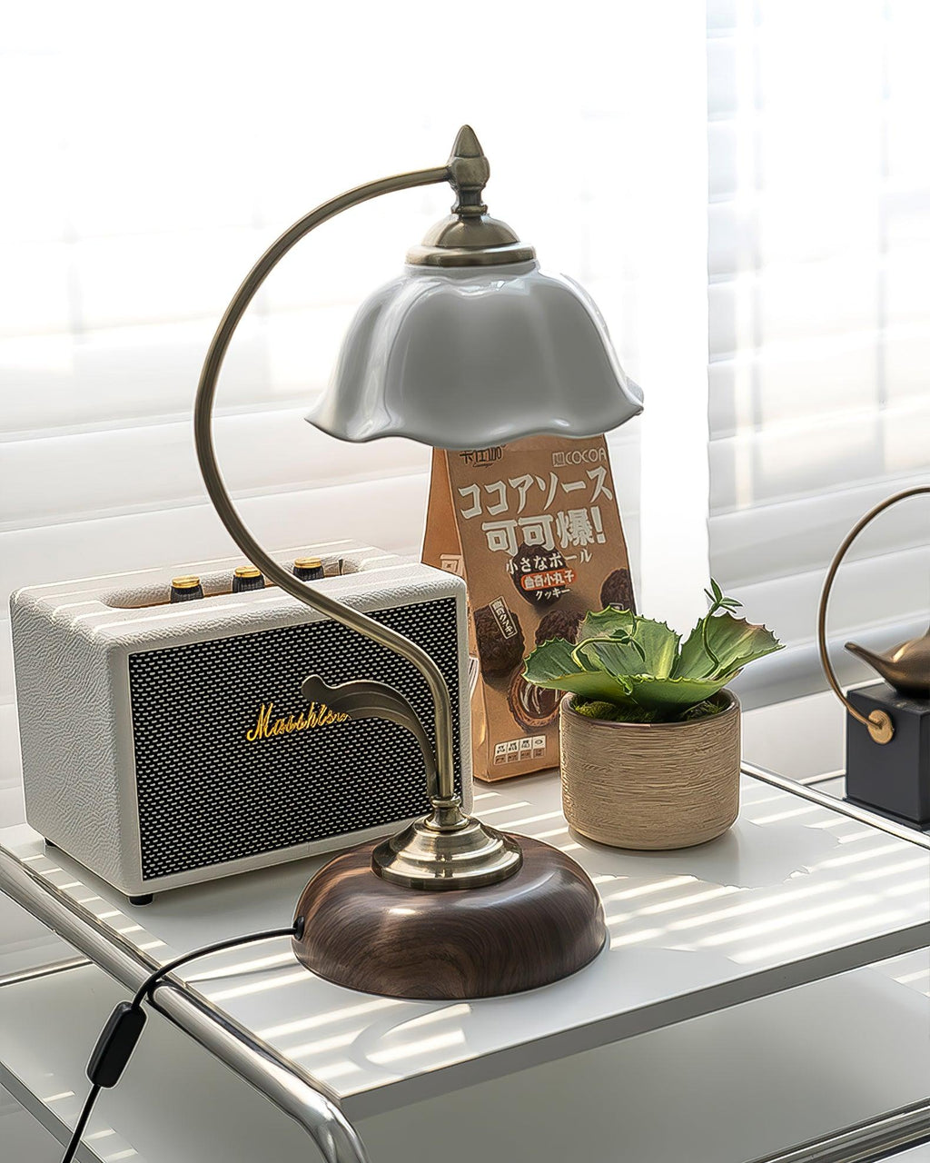 Clérachic lamp with its curved arm and white ceramic shade, seen from low down beside a cream speaker and a potted succulent.