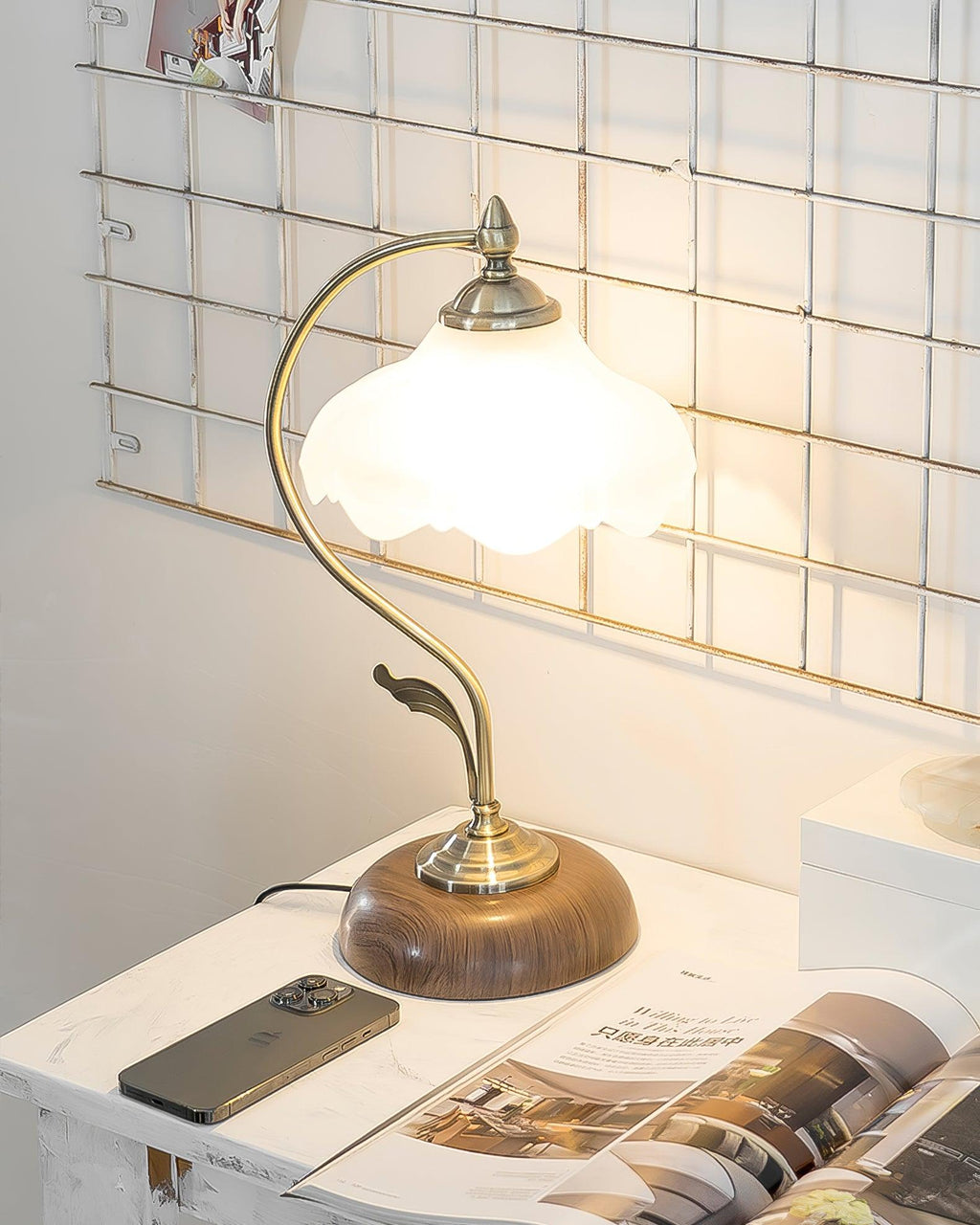 Clérachic table lamp lit on a marble-topped surface, with a phone and an open magazine in front of a metal wall grid.