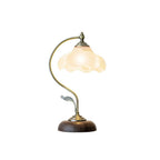 Lit Clérachic table lamp with a frosted glass flower shade and a leaf detail on its arm, shown on a white backdrop.
