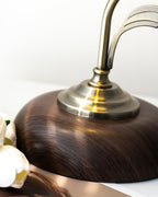 Close view of the brass-toned collar and the walnut-effect wood-grain base on this Clérachic table lamp, with white tulips beside it.