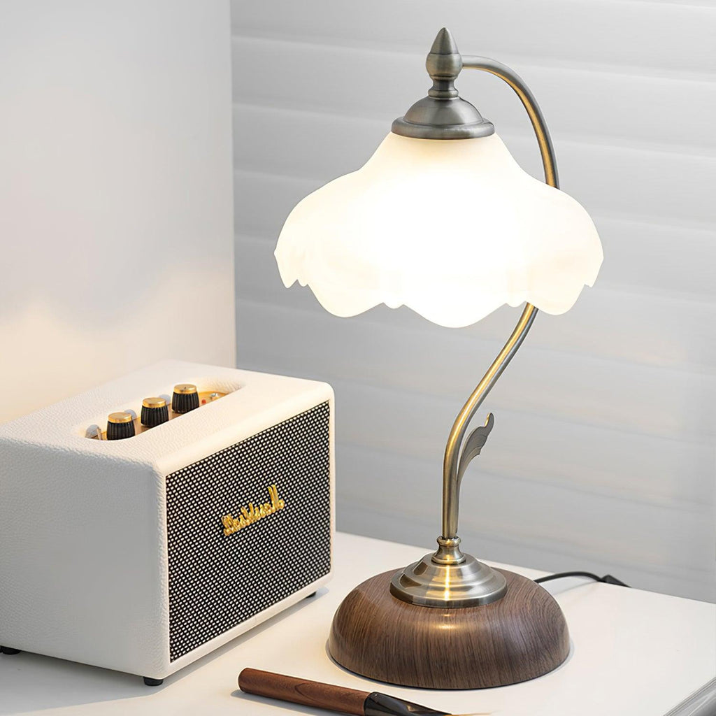 Frosted glass shade of this Clérachic table lamp lit up beside a cream speaker on a white desk, with a window blind behind.