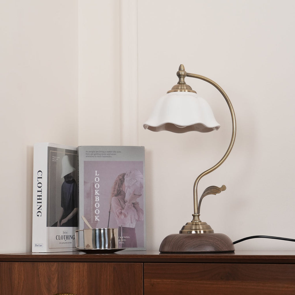 Clérachic table lamp with a white ceramic shade, standing on a wooden sideboard in front of a clothing book and a lookbook.