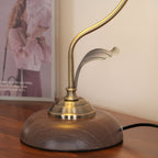 Close view of the leaf detail, brass-toned collar and wood-grain base of this Clérachic table lamp on a polished wooden sideboard.
