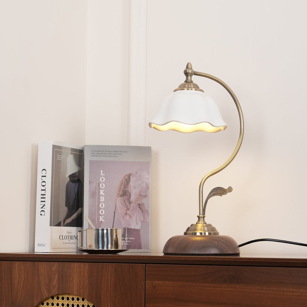 Clérachic table lamp lit on a sideboard in a cream room, its ceramic shade glowing at the rim beside books and a steel cup.
