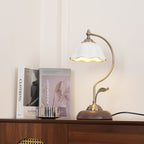 Clérachic table lamp lit on a sideboard in a cream room, its ceramic shade glowing at the rim beside books and a steel cup.
