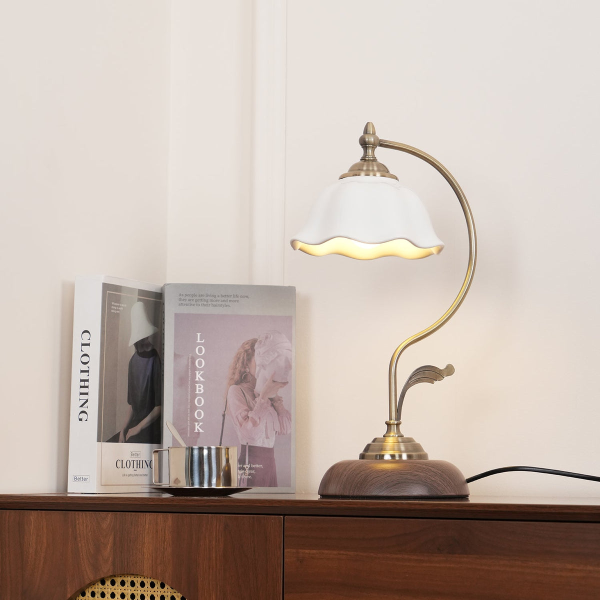 Clérachic table lamp lit on a sideboard in a cream room, its ceramic shade glowing at the rim beside books and a steel cup.