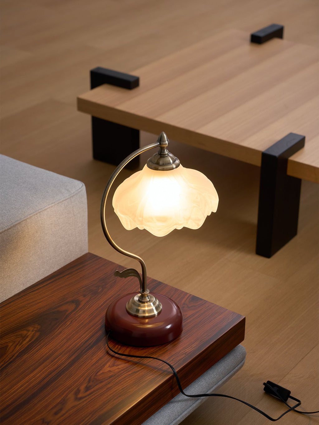 Lit Clérachic table lamp with a frosted glass shade, set low on a dark wood table with a switch on its cord, beside a grey sofa.
