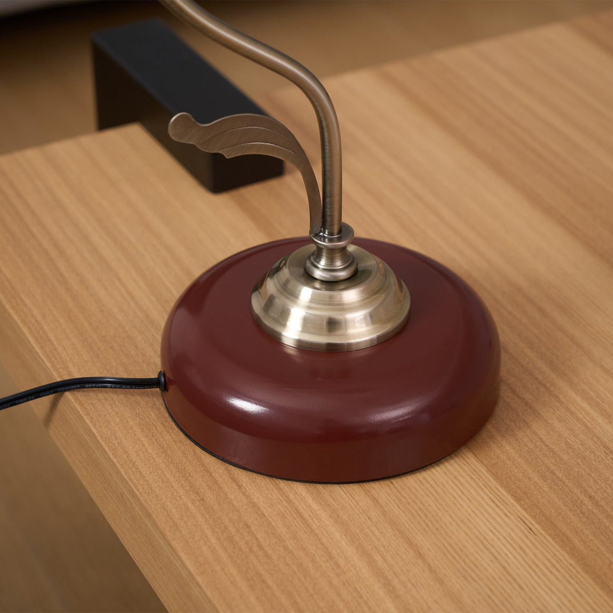 Close view of the round base and brass-toned collar of this Clérachic table lamp on a light oak surface, with its black cord.