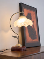 Lit Clérachic table lamp with a frosted glass shade, in front of a large framed print of a dark cat on an orange ground.