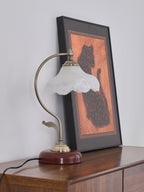 Unlit Clérachic table lamp with a frosted glass shade, leaning against a framed cat print on a dark wooden sideboard.