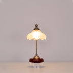 Lit Clérachic table lamp with a straight stem and a warm glowing glass shade on a clear block against a soft grey wall.