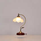 Clérachic table lamp lit against a grey wall, its curved arm and leaf detail rising from a round base on a clear acrylic plinth.