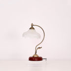 Unlit Clérachic table lamp with a milky glass shade and a curved brass-toned arm, photographed on a plain light backdrop.