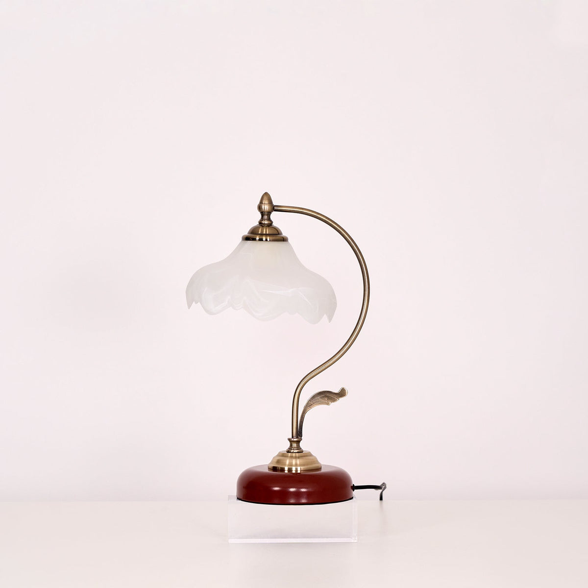 Unlit Clérachic table lamp with a milky glass shade and a curved brass-toned arm, photographed on a plain light backdrop.