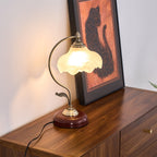 Lit Clérachic table lamp on a dark wood chest of drawers, beside a framed cat print and a cord trailing down the side.