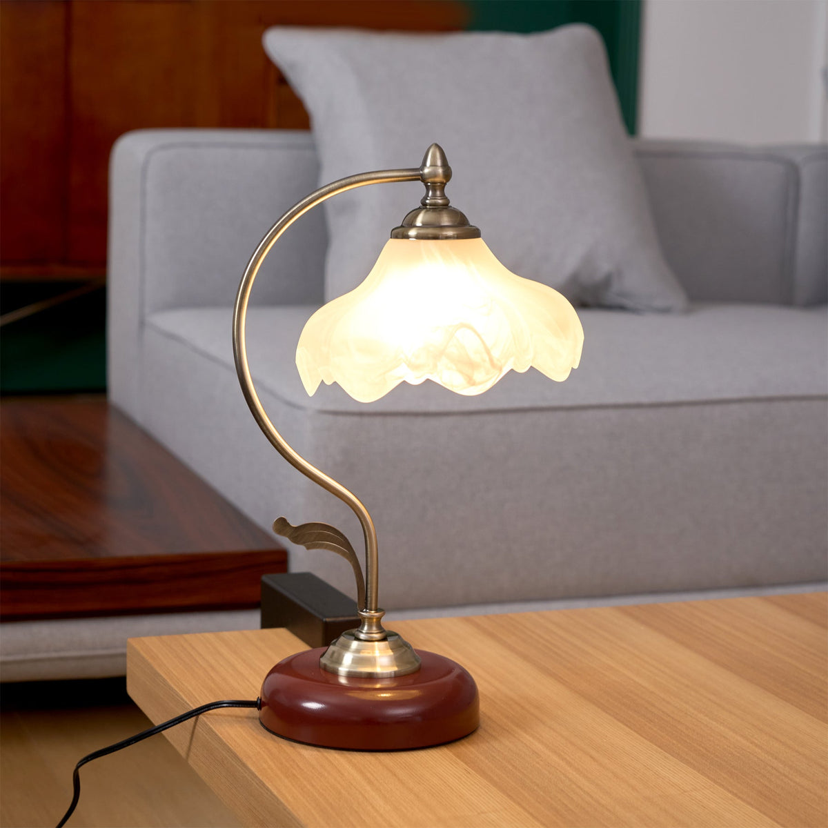 Clérachic table lamp glowing on a light oak table in front of a grey sofa with a cushion, with a black switch beside its base.