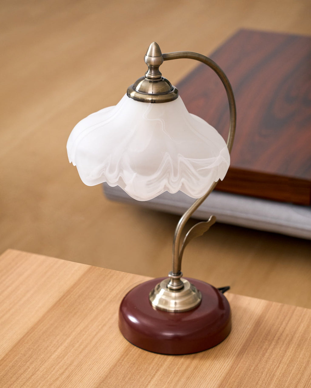 Close view of the frosted glass shade and brass-toned arm of this unlit Clérachic table lamp, on a light oak table.