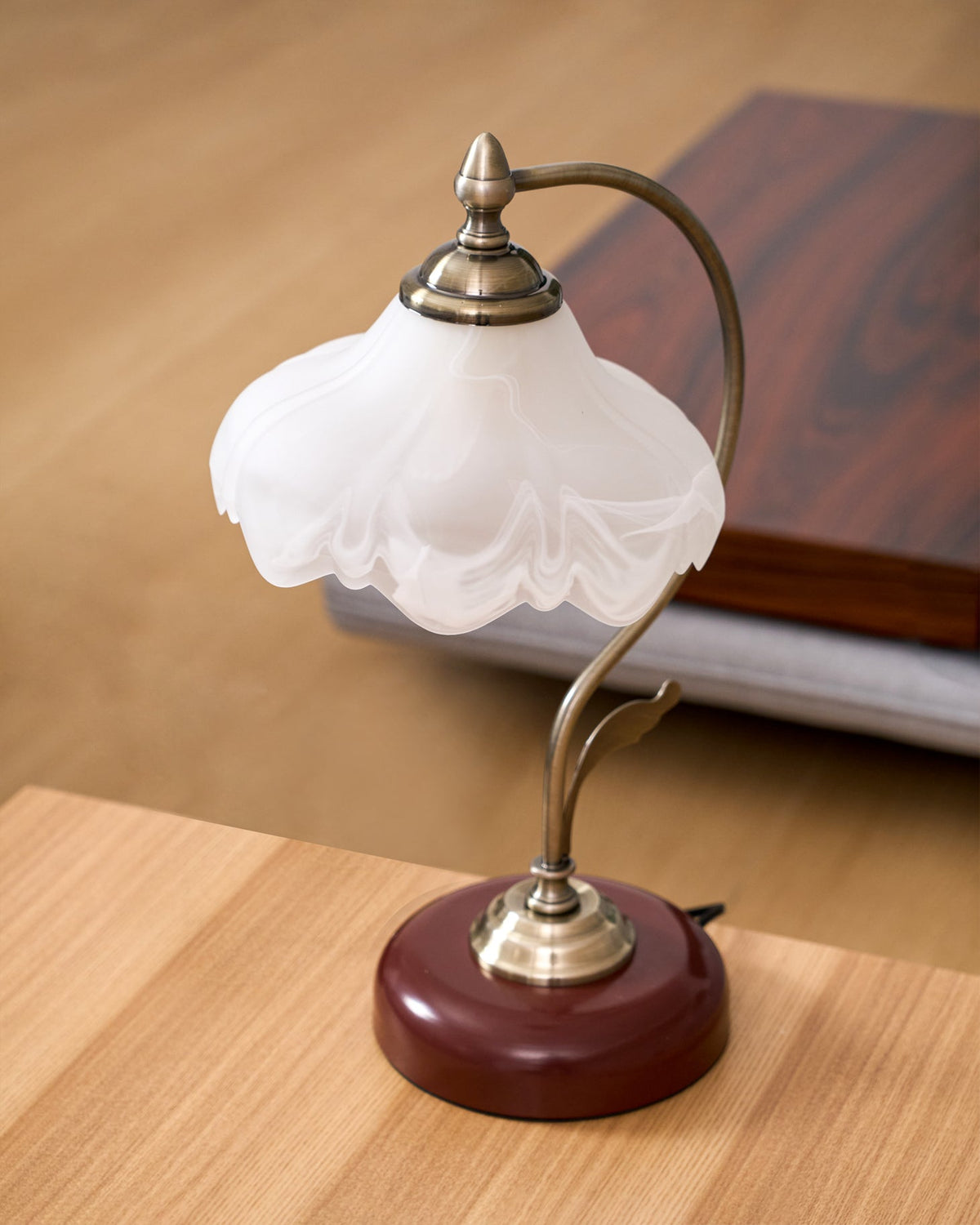 Close view of the frosted glass shade and brass-toned arm of this unlit Clérachic table lamp, on a light oak table.