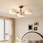 This Clérachic ceiling light glows warmly above a cream-panelled bedroom with a black arched headboard and sheer curtains.
